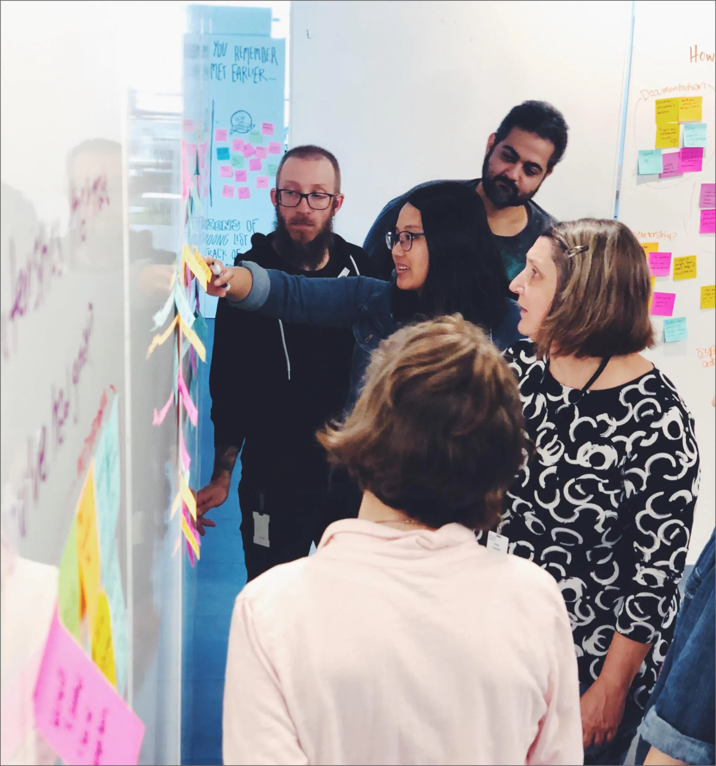 group of people looking at whiteboard covered with post it notes showing user research